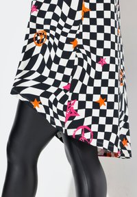 Zwart-wit geblokte jurk met roze en oranje sterren en vredesymbolen, met een vloeiende ontwerpen en een high-low zoom. Zwarte legging eronder.