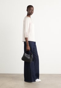 Black woven handbag with a rounded handle, paired with a light pink blouse and wide-leg dark denim jeans, worn with white sneakers.
