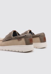 Zapatillas en beige y oliva con parte superior de ante y sintético, punta redonda, suela de goma blanca y ojetes decorativos. Acento de logo en cuero marrón.