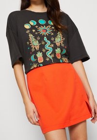 Svart oversized t-shirt med färggrafisk design av sol, orm och ananaser. Matchas med en ljusorange minikjol med sidoslits.