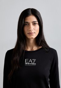 Zwarte longsleeve gemaakt van zachte stof, met een metallic zilveren logo "EA7 EMPORIO ARMANI" gecentreerd op de borst.
