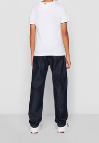 Camiseta de algodón blanca de manga corta, combinada con jeans de mezclilla azul oscuro. Zapatillas con acentos en rojo, blanco y negro completan el atuendo.