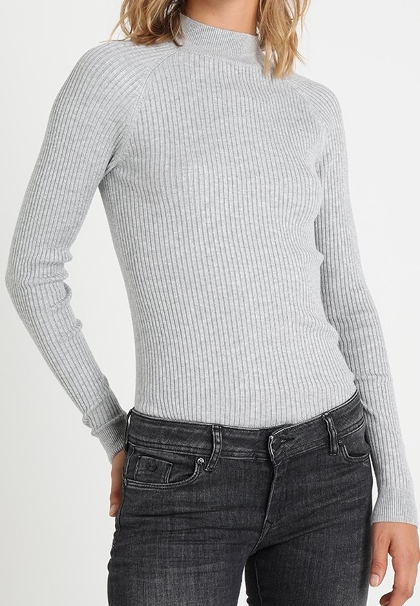 Haut gris clair à manches longues côtelées avec un col montant et une coupe ajustée, associé à un jean foncé. La texture est douce et extensible.