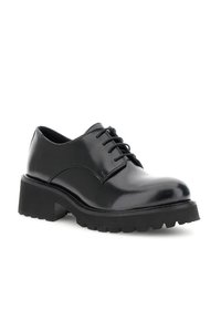 Scarpa in pelle nera lucida con lacci, suola spessa e tassellata e tacco basso, inclinata leggermente a destra su sfondo bianco.