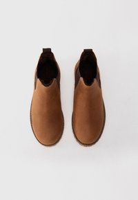Une paire de chaussures en cuir brun à enfiler avec des semelles surpiquées, vues de dessus sur un fond blanc.