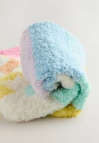 Gerollte, weich strukturierte Decken in Pastellfarben, einschließlich Blau, Lavendel, Weiß, Gelb und Rosa, auf einer hellen Oberfläche.