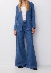 Denim blazer, light blue, structured design with lapels and two front pockets. Paired with wide-leg matching denim pants.