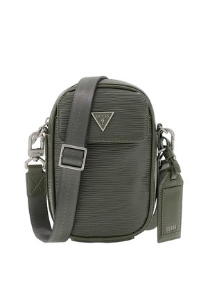 Kompaktní tmavě zelená texturovaná kabelka přes rameno s nastavitelným popruhem, stříbrným kováním, destičkou s logem Guess a připojenou zavazadlovou visačkou.