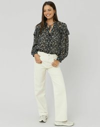Blouse noire à imprimé floral avec des manches volantes et un détail de col noué, associée à un jean large crème et des baskets gris clair.