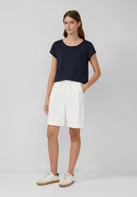Granatowa, krótka koszulka, białe szorty z plisami i jasne trampki z beżową podeszwą. Prosty design, miękka tkanina i luźny krój.