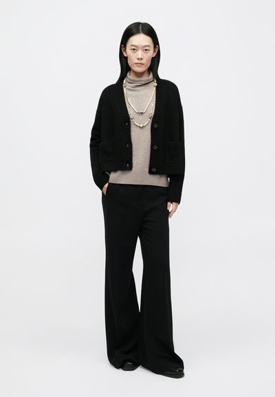 Μαύρη ζακέτα με ραβδώσεις και μπροστινές τσέπες, πάνω από μπεζ ζιβάγκο. Φαρδιά μαύρη παντελόνα και στρωματοποιημένο κολιέ με πέρλες ολοκληρώνουν την εμφάνιση.