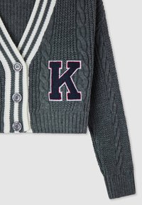 Cardigan lavorato a maglia grigio scuro con bordino a strisce bianche, tre bottoni e grande toppa con la lettera "K" blu navy sul davanti.