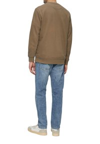 Bruine sweatshirt met ronde hals, gecombineerd met lichtblauwe jeans en witte sneakers. Voorzien van ribgebreide manchetten en zoom, gladde textuur.