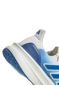Baskets Adidas Ultraboost blanches et bleues, inclinées pour montrer la semelle texturée et la languette de talon avec logo sur fond blanc.