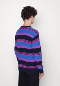 Randig tröja i flera färger som har blå, lila och svarta nyanser med röda accenter; stickad textur och ribbade ärmslut och nederkant.