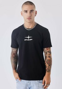 Zwarte korte mouwen t-shirt met een wit gedrukt logo "PXP" op de borst, gemaakt van zachte stof. Gepaard met lichtblauwe denim shorts.