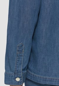 Denimjacke mit dunkelschwarzem Ärmelsaum; ausgestattet mit einem Knopfverschluss, spitzem Saum und sichtbaren Nähten auf dem Stoff. Strukturierten Oberfläche.
