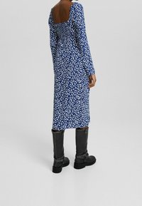 Long-sleeved blue dress with white floral pattern, smocked back, and a square neckline, paired with black knee-high boots featuring buckles.