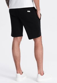 Shorts neri in cotone con vestibilità comoda, con tasche laterali e un piccolo etichetta sulla parte posteriore. Abbinati a sneakers bianche.