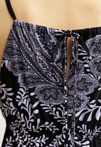 Svart- och vitmönstrad klänning med tunna axelband, knytning bak och blommönster med intrikata detaljer och en mjuk textur.