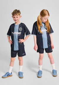 Marinblå och ljusblå sportkläder bestående av en kortärmad tröja med ränder och logotyp, ihop med matchande shorts och blå sportskor.