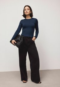 Navy long-sleeve top paired with high-waisted black wide-leg jeans. Black pouch bag with a gathered design. Model wearing flat sandals.