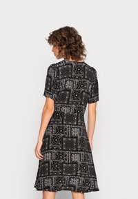 Vestido preto de mangas curtas com um detalhado padrão paisley e geométrico em branco. Saia evasé e decote redondo. Tecido suave com um ligeiro brilho.