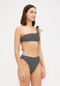 Bikini z vzorcem v črno-beli kombinaciji, z enostranskim zgornjim delom z mašno in visokim pasom, gladka tekstura tkanine.