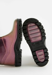 Fialové iridescentní gumové kotníkové boty s texturovanou černou podrážkou se žebrovaným a kulatým akcentem. Hladký povrch s jemným gradientem.