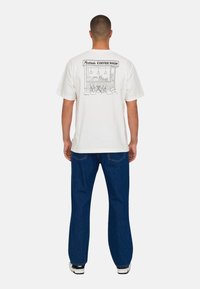 Witte katoenen t-shirt met een lijntekening van een koffiehuis op de achterkant. Gecombineerd met donkerblauwe jeans en sneakers.