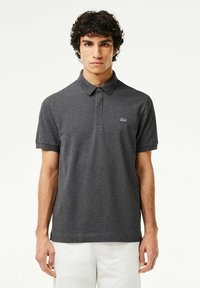 Mörkgrå pikétröja med krage, korta ärmar och en diskret broderad logotyp på vänster bröst. Slät textur, lätt tyg.