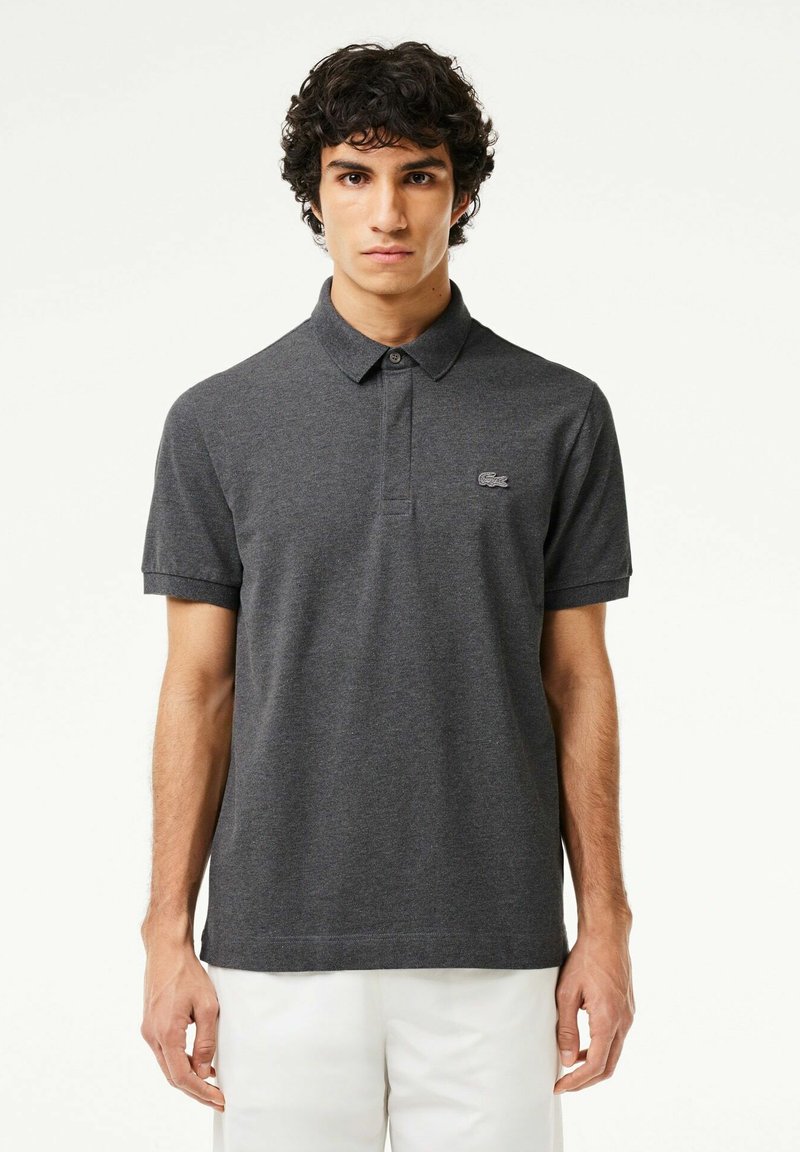 Mörkgrå pikétröja med krage, korta ärmar och en diskret broderad logotyp på vänster bröst. Slät textur, lätt tyg.