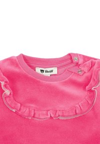 Top de terciopelo rosa con un escote con volantes y un ribete plateado, y cierre a presión en el hombro; etiqueta de marca visible en el interior.