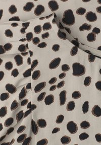 Tissu beige avec motif léopard irrégulier noir et marron et coutures visibles sur les bords pliés du vêtement.
