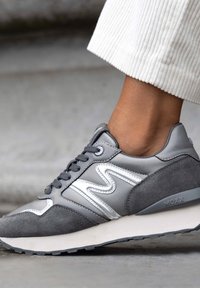 Sneaker grigio con tomaia in pelle liscia e dettagli in suede. Presenta un design a zigzag bianco, lacci grigi e una suola in gomma testurizzata.