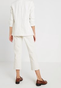 Blazer rayé blanc, pantalon cropped crème, et chaussures en cuir marron. Le blazer a des manches retroussées, et le pantalon a une coupe droite.