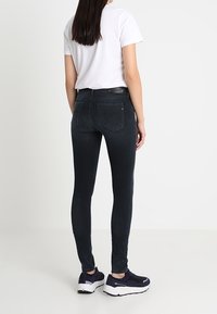 Mustat skinny-farkut, valmistettu denimistä, joissa on kapea istuvuus, normaalit taskut ja keskileveä vyötärö, yhdistettynä valkoiseen t-paitaan ja laivastonsinisiin tennareihin.