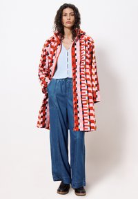 Colorful long coat with geometric patterns in red, pink, and blue, paired with light blue top and loose denim pants. Heavy-soled shoes.