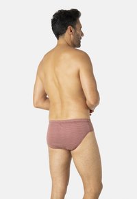 Slip de bain rouge à motifs en tissu léger, avec une coupe ajustée et une texture lisse, doté d'une ceinture unie et d'une couverture minimale.