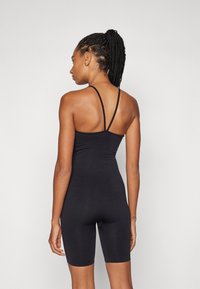 Svart ribbet body med tynne spaghetti-stropper, med en tettsittende design og midt på låret lengde, som viser en jevn, elastisk tekstur.