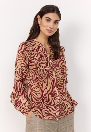 A light, textured blouse features a red and beige zebra pattern with ruffles along the front and sleeves. It has a deep V-neckline.