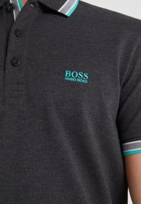 Mörkgrå pikétröja i strukturerad tyg, med en tre-knappsknäppning, broderad "BOSS"-logga i turkos och randiga accenter vid kragen.