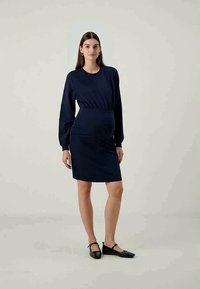 Vestido azul-marinho com mangas longas e bufantes, cintura ajustada e comprimento até aos joelhos. Feito de um tecido suave sem padrões visíveis ou detalhes em metal.