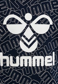 Tissu bleu marine avec un design graphique blanc présentant un visage abstrait et le mot "hummel," entouré d'un motif linéaire blanc.