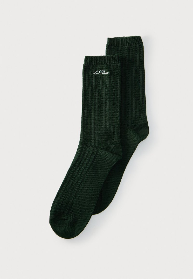 Paire de chaussettes côtelées vert foncé avec logo "Les Deux" brodé en blanc près du bord supérieur, présentées à plat sur un fond clair.