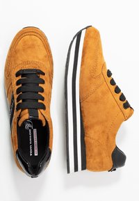 Zapatillas de ante naranja con detalles en negro, puntera redonda, cordones negros y una suela blanca a rayas. Cuenta con una plantilla de espuma viscoelástica para mayor comodidad.