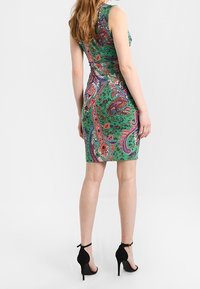 Grön klänning med paisleymönster, med en åtsittande design, ärmlös klippning och knä-lång fåll. Accentuerad med svarta högklackade sandaler.