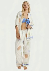 Lightweight, cream-colored fabric set featuring a kimono-style open shirt with sun patterns, paired with blue ribbed bikini and loose pants.