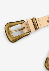 Cintura in pelle di un leggero pesca con una fibbia decorativa in ottone invecchiato. Presenta una cucitura dettagliata lungo i bordi e una texture liscia.