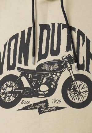 Haut à capuche beige avec un graphisme de moto noir, comprenant un œil ailé, et du texte « Von Dutch » en gras en haut, suivi de « Since 1929 Amazing Kustom » en bas.